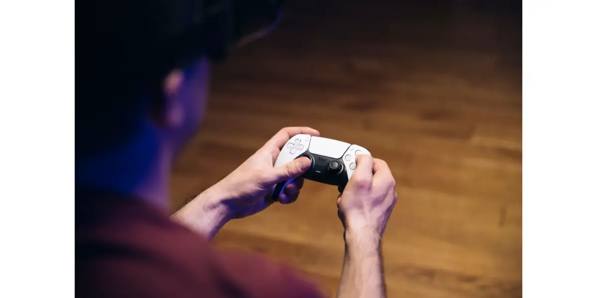 Adobestock_423058964 Крупным планом рук мужчины, играющих в видеоигры на игровой консоли перед телевизором, широкоэкранный, используя контроллер PS5