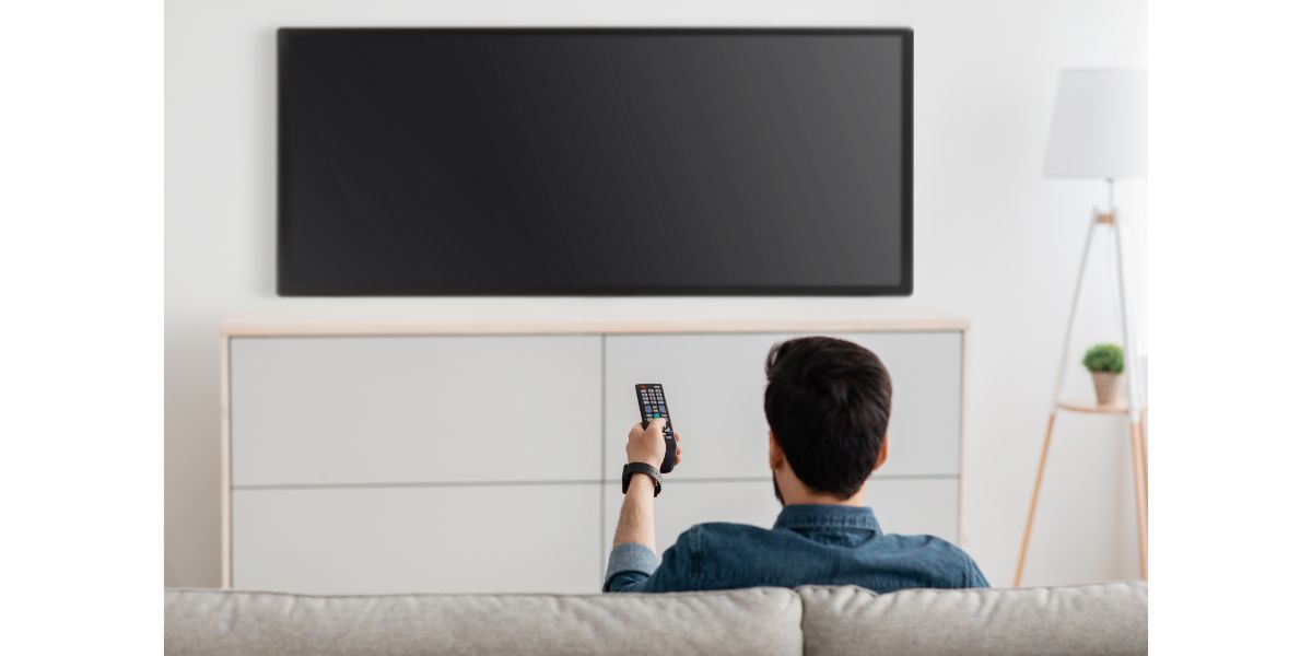 AdobeStock_430594212 Man watching television, turning on plasma flatscreen TV-set, pointing remote control at empty TV screen on white wall