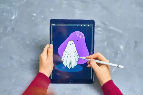 AdobeStock_436412964_Editorial_Use_Only Woman Illustrator draws Ghost on iPad Pro in procreate program using apple pencil. Digital Illustrator. Freelance work as a designer.