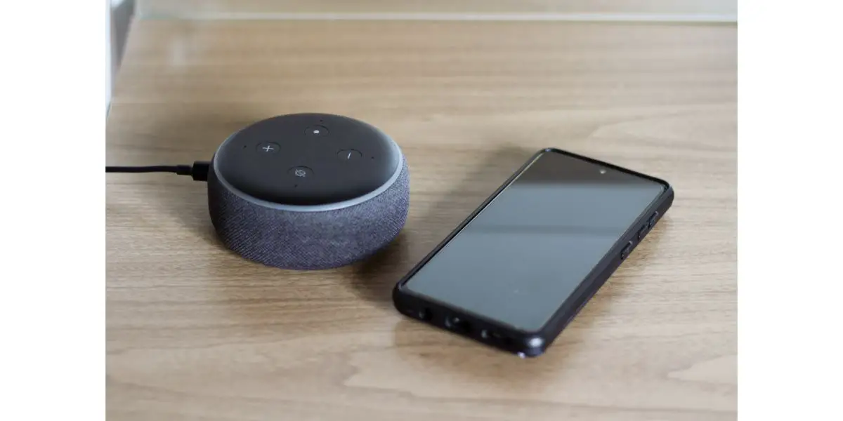 AdobeStock_437310803 Alexa device and phone on wooden desk