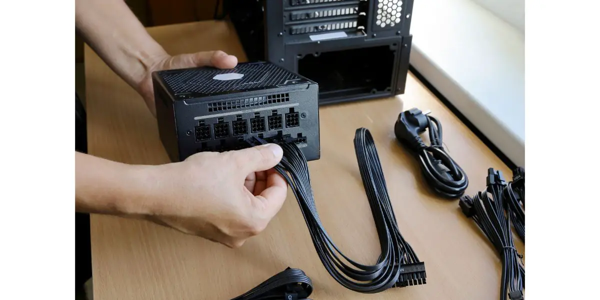 AdobeStock_448602886 Hands connect wires to power supply unit while assembling computer system