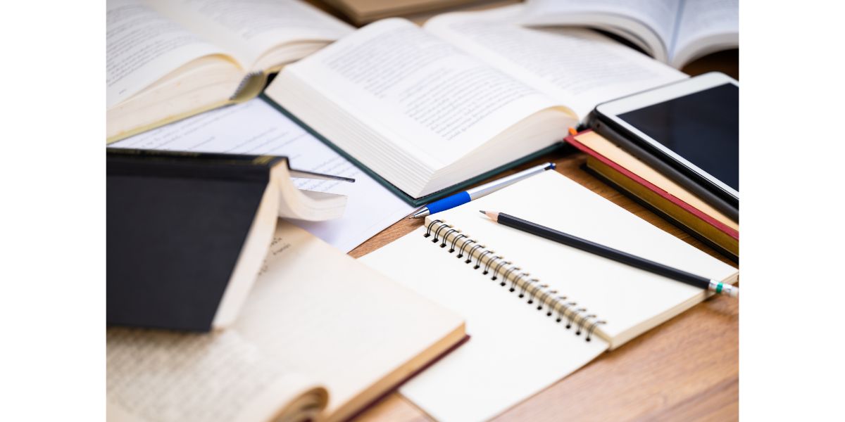 AdobeStock_468966481 Closeup pencil on the notebook with many opened books on the desk, editing or rewrite the information from many reference book to create a new content