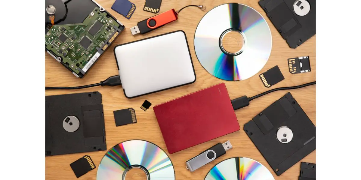 AdobeStock_488017836 Data storage devices such as CDs, hard drives, pen drives and other, top view on a wooden background