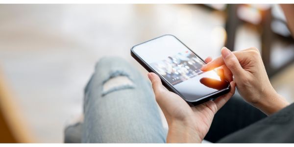 AdobeStock_492504281 Cropped image of woman hand holding smartphone and watching video with night bokeh background.