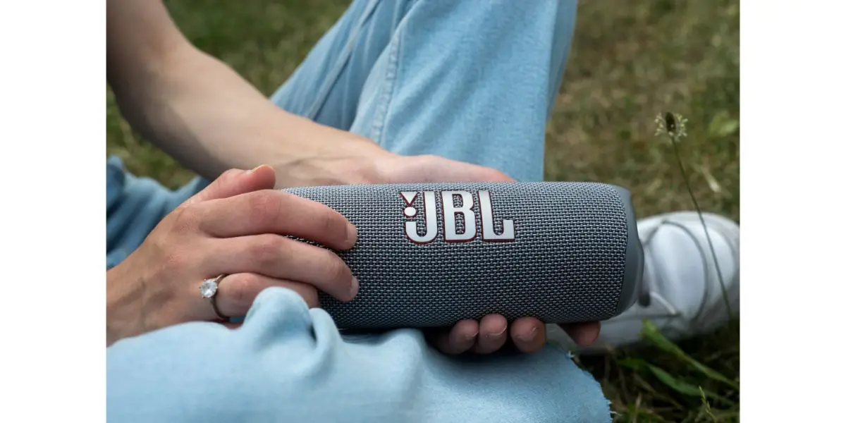 AdobeStock_511595377_Editorial_Use_Only Closeup of grey portable JBL subwoofer speaker in hands of young woman sitting in a public garden