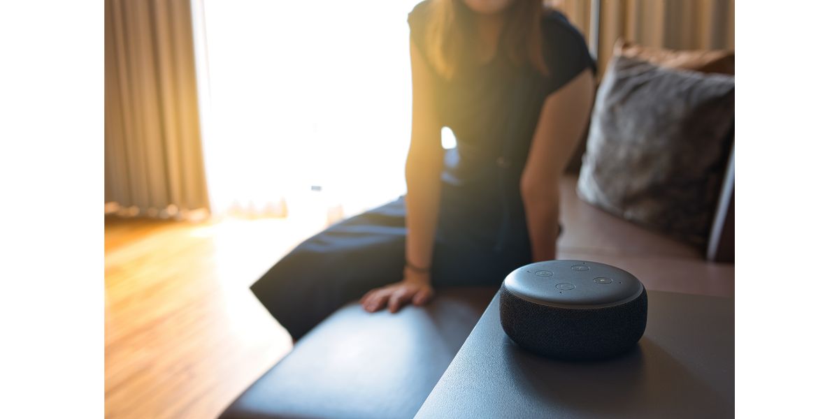 AdobeStock_539193172 Woman sitting on a chair and talking to a speech recognition device, Amazon Alexa with sunlight background