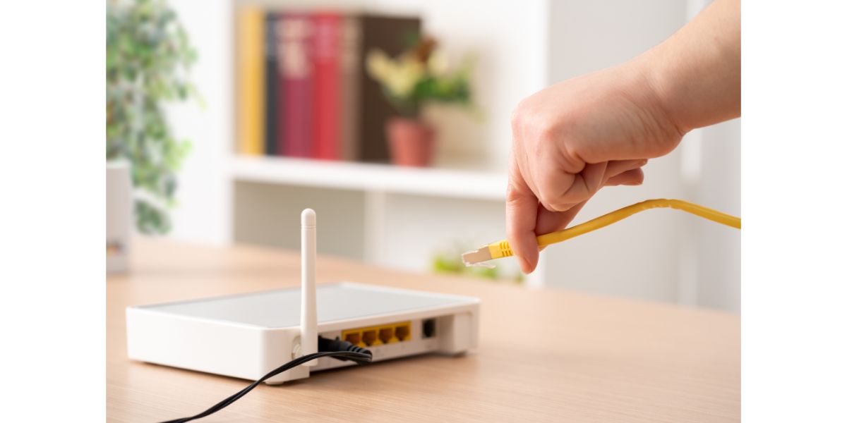 AdobeStock_571740066 Close up of man hand plugging ethernet cable to router on a desk at home