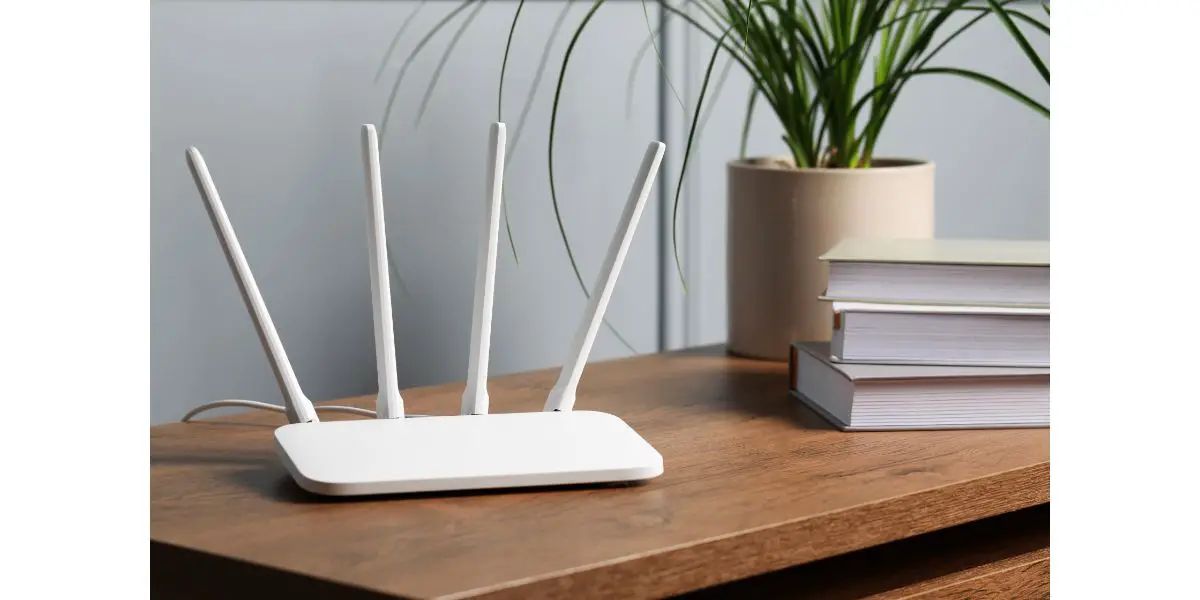 AdobeStock_572814102 New white Wi-Fi router on wooden table next to books and a plant indoors