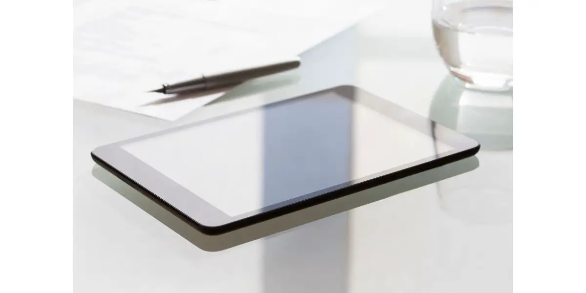 AdobeStock_92160136 Digital tablet on modern glass table in office near pen paper and glass of water on a clear table
