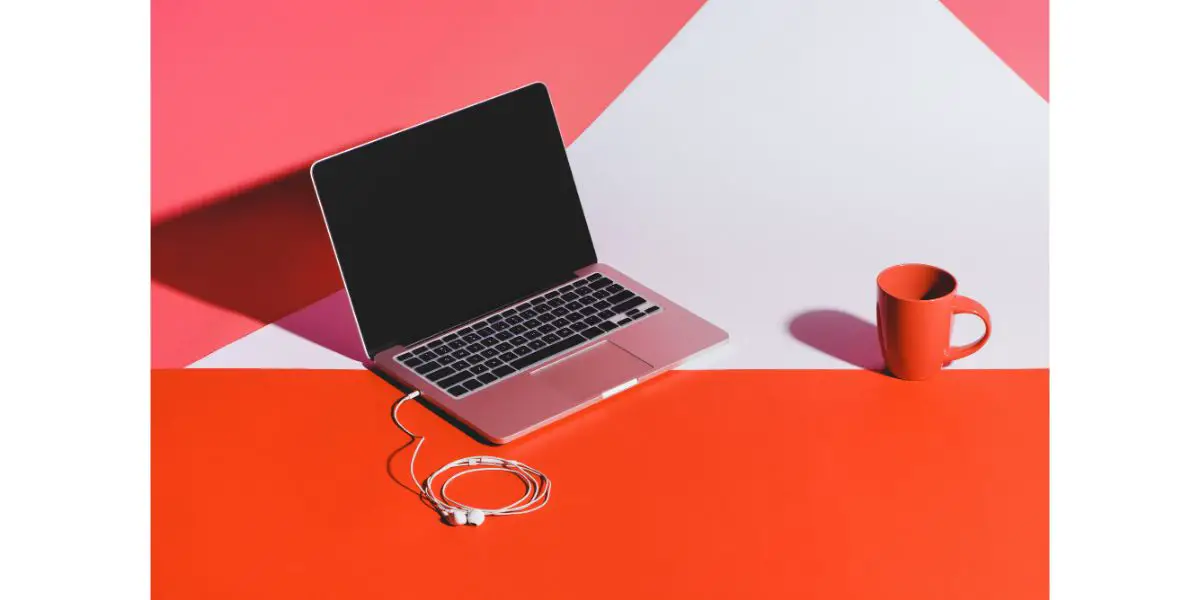 Depositphotos_165210806_L redish orange Coffee cup , earphones plugged into laptop on light red, white and red background