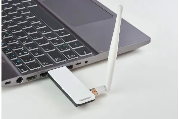 Depositphotos_189723426_S Silver laptop with USB modem plugged in with an antenna, on a white board table