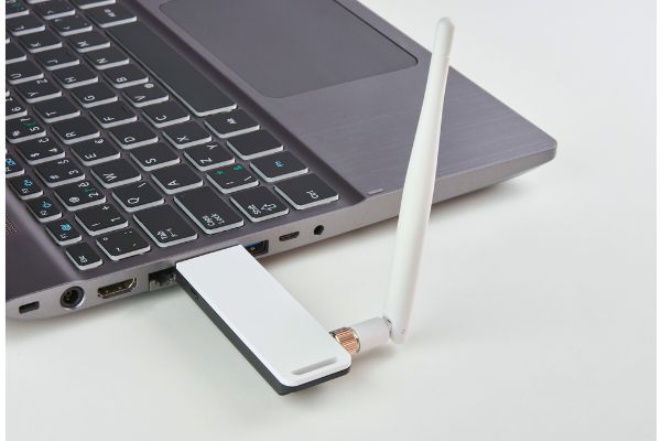 Depositphotos_189723426_S Silver laptop with USB modem plugged in with an antenna, on a white board table