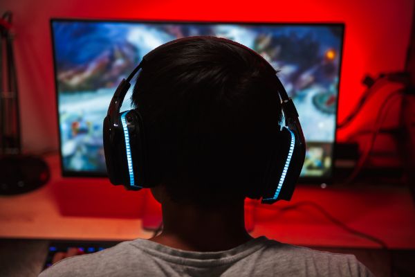 Depositphotos_211746204_S Portrait from back of young gamer guy looking at screen and playing video games on computer in dark room wearing headphones