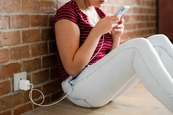 Depositphotos_242594298_S Teen girl using her phone while charging the batteries