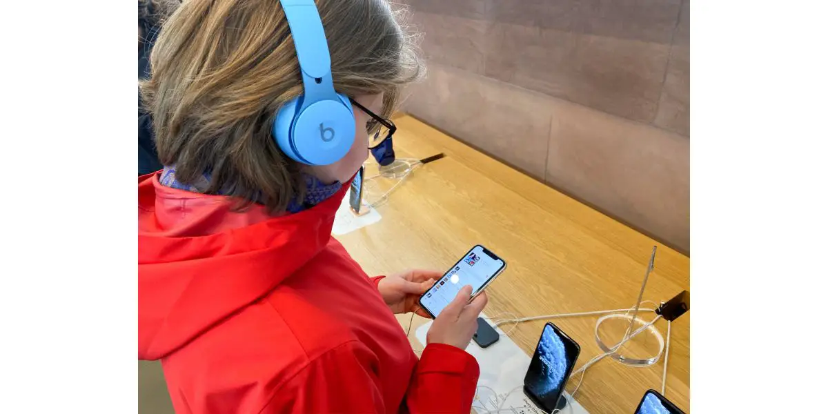 Side view woman in red coat inside Apple Computers Store testing listening to music with new latest Blue Beats by Dr Dre Solo Pro Active Noise Cancelling headphones