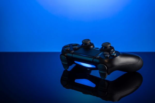 Depositphotos_364337174_S Black gamepad with backlight on blue background. Joystick on glossy surface