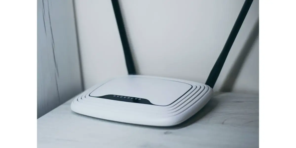 white router with two antennas ontop of a white table against the wall