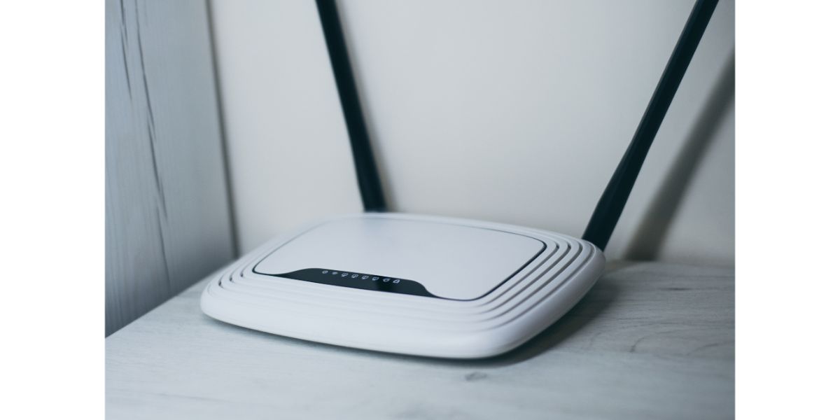 white router with two antennas ontop of a white table against the wall