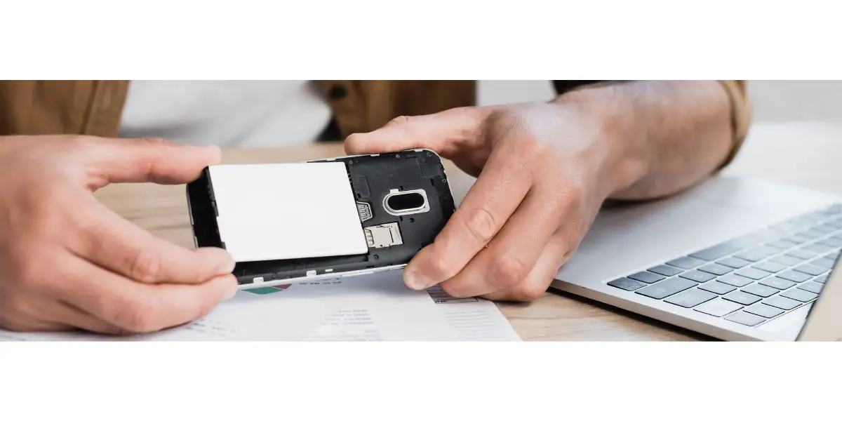 Depositphotos_422387732_L businessman changing phone battery on wooden desk next to laptop