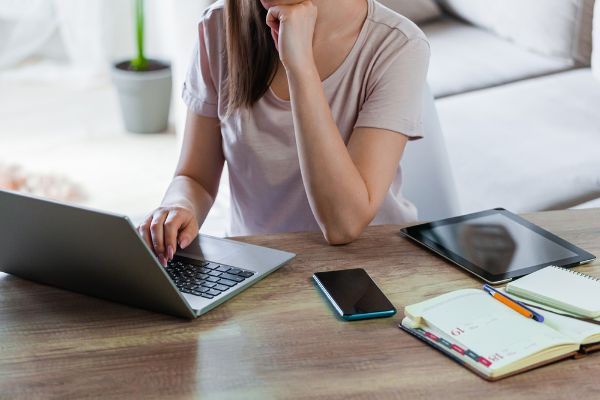 Depositphotos_461456082_S Young woman using laptop to work at home, multiple devices