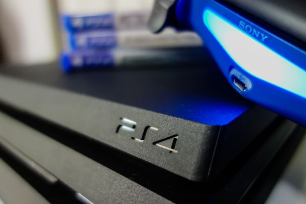 Depositphotos_471828314_S Sony black Playstation 4 Pro game console and blue wireless controller. PS4 symbol