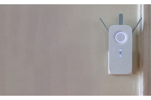 Depositphotos_573841646_S Wifi Extender at power outlet on grey empty wall background. Wireless repeater home device, network booster, router antenna