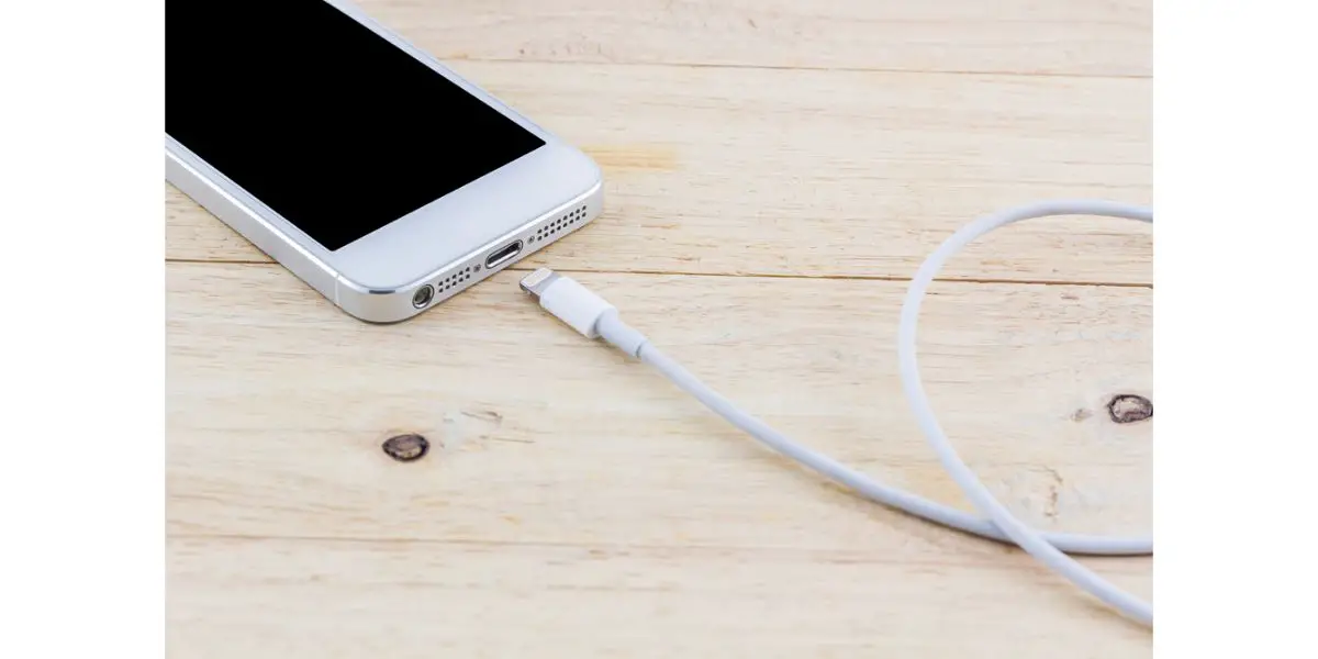 Depositphotos_78858200_S old smartphone on light wood table showing charge port and a charging cable about to be plugged in